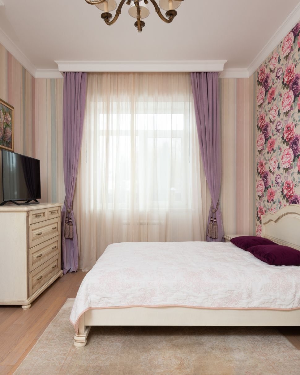 Bedroom with a pink floral wallpaper accent wall behind an upholstered bed