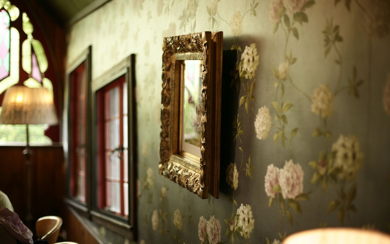 Interior with green floral wallpaper, a gilded mirror, and soft natural light